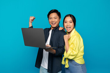 Glad millennial asian couple in casual rise fist, celebrate win, success with laptop