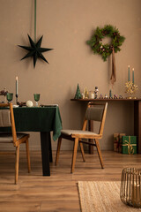 Interior design of warm dinning room interior with christmas table, wooden console, christmas gifts, gingerbread, candle, star on wall christmas wreath and personal accessories. Home decor. Template. - obrazy, fototapety, plakaty