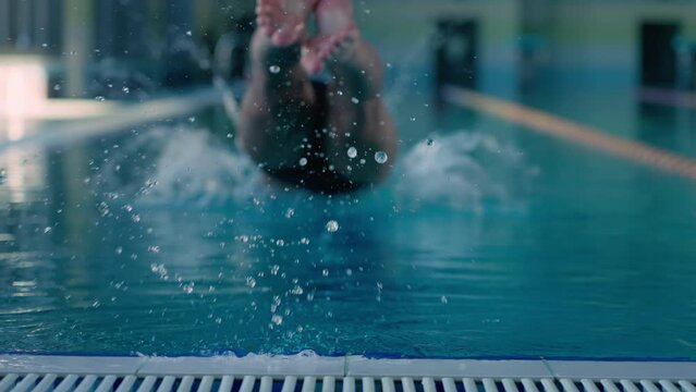 Barefoot swimmer jumps in clear pool water from edge at training