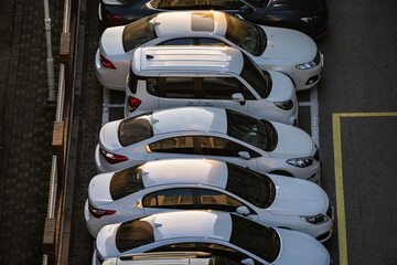 Top angle view of several cars parked in an outdoor parking lot with sunlight and shadows on the...