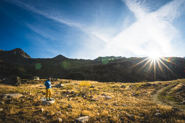 Bergsteiger mit blauer Jacke und Kaffee schaut in die aufgehende Sonne