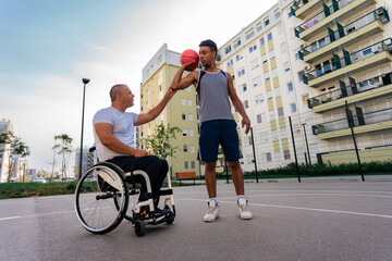 Mature man in the wheelchair coaching basketball to a young black man at the youth center before tryouts