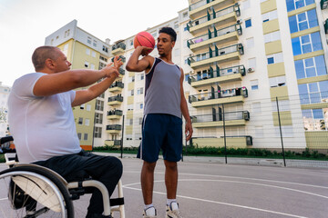 Mature man in the wheelchair coaching basketball to a young black man at the youth center before tryouts