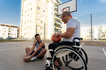 A young black man stretches as he has a conversation with an older man in wheelchair before or after a friendly one-on-one game of basketball