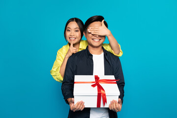 Smiling millennial asian woman in casual closed eyes to man, hold gift box with present