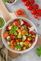 Caprese salad with cherry tomatoes, mini mozzarella balls, avocado, pesto sauce and fresh basil. Healthy vegetarian meal.