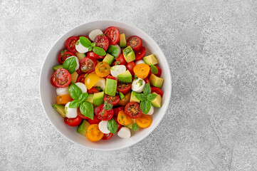 Caprese salad with cherry tomatoes, mini mozzarella balls, avocado, pesto sauce and fresh basil. Healthy vegetarian meal.