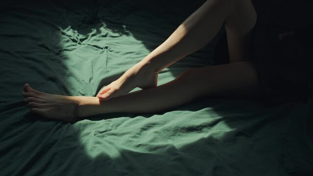 Female legs gently rub against each other. Pan up to attractive woman legs in bed, comfort and relaxation concept. Cinematic scene