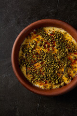 Close-up vertical top view of crème brûlée, highlighting its caramelized crust and pistachio garnish, elegantly poised in a clay bowl