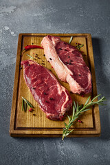 Vertical side perspective highlighting the raw allure of striploin and New York steaks resting on a wooden board, perfectly contrasted by a gray background