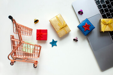 Shopping cart, gift boxes, laptop on the white background. Christmas shopping online. Top view.