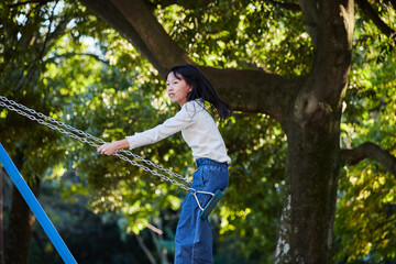 秋の公園でブランコを遊んでいる小学生の女の子の様子 - obrazy, fototapety, plakaty