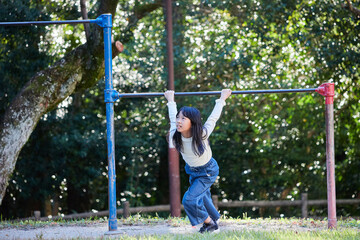 Fototapeta premium 秋の公園で鉄棒を遊んでいる小学生の女の子の様子
