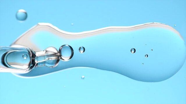 Cosmetic dropper with serum, beauty cosmetics dripping, on blue background. Macro shot. Serum, peptides, beauty and health care products. Glass pipette with liquid close up. Top view. Skin care 