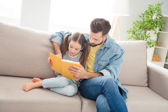 Photo of man hands hold book reading with adorable positive girl sit on couch enjoy free time vacation indoors