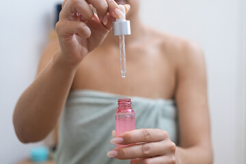 Radiant skin: Near her mirror, a woman perfects her anti-aging skincare by applying hyaluronic acid with a serum dropper. 