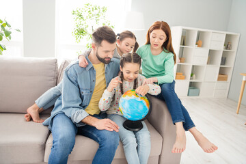 Photo of four people handsome guy adorable girls sit on couch fingers pointing spinning globe weekend indoors