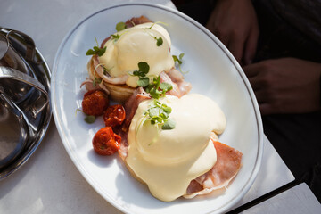 Eggs Benedict common American breakfast or brunch dish, consisting of two halves of an English muffin, each topped with Canadian bacon, a poached egg, and hollandaise sauce.