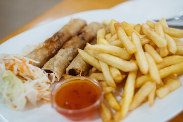 Crunchy Asian appetizer - deep fried spring rolls stuffed with vegetables with  hot chili sauce and french fries