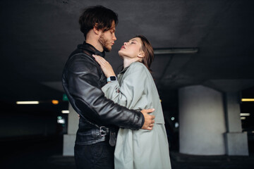 man in a leather jacket and a woman in a coat hugging in an underground parking lot, a couple in love on a date.