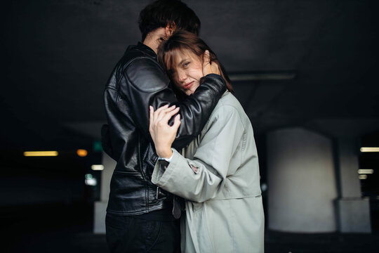 man in a leather jacket and a woman in a coat hugging in an underground parking lot, a couple in love on a date.