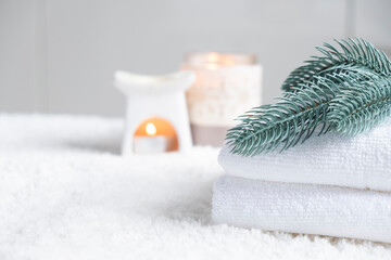 Fototapeta na wymiar Fresh white towels with fir branch, candles and Christmas decorations. Wellness and wellbeing. SPA massage or beauty salon, relaxation and self care in Christmas or New Year variant. Copy space.