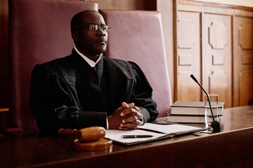 Serious male impartial judge in uniform sitting by desk in front of microphone and keeping his...