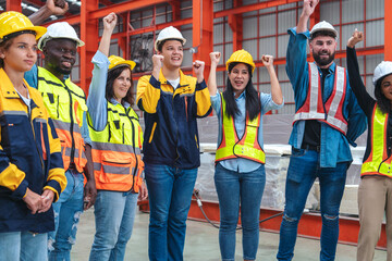 A group of male employees, engineers and female workers wearing uniform jackets, working together in unity, happy to work successfully, happy to raise their hands in the factory.