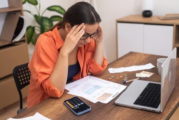 Fotobehang Financial Confusion: In glasses, a stressed woman at a table looks at paper bills, perplexed by the high payment rates.  © olga_demina