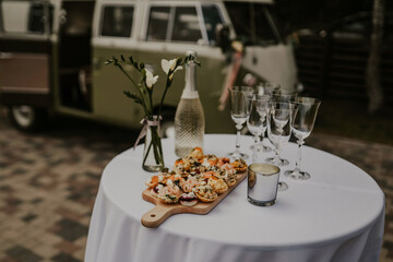 A wedding snack table, set up like a restaurant, in the midst of the forest, adorned with delectable treats, while a car is parked in the background