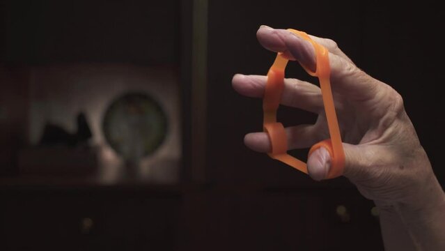 Old woman training her fingers with rubber exercise machine. Hand close-up. 