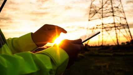 Silhouette of engineer man using tablet checking high-voltage power lines.