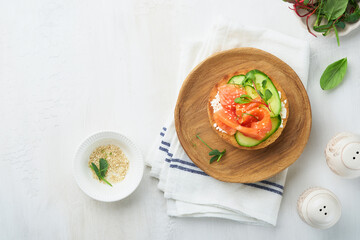 Open smoked salmon sandwiches with cream cheese, cucumber, sesame seeds, microgreens, spinach, and peas leaves on light old wooden background. Healthy breakfast food. Delicious snack. Top view.