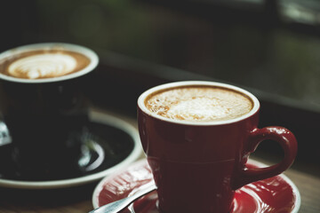 Two cup tea or coffee on wooden table side view window.Red and black hot coffee cup on the table by the window on a rainy day.Side view mugs on glass with reflection in the cafe on vintage style.