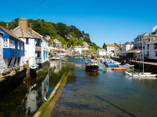 Fototapeta na wymiar Sailing and fishing boats in harbour at the coastal village and port of Polperro on the south coast of Cornwall, UK. White and blue houses, hillside, clear blue sky.