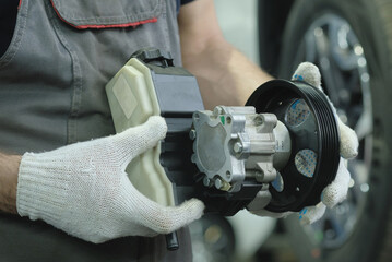 A new hydraulic pump in the hands of an auto mechanic. A mechanic at a car service center monitors the serviceability of the hydraulic power steering before replacing it.