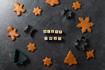 Fotobehang holidays, cooking and baking concept - close up of merry christmas words made of wooden toy blocks or stams, gingerbread cookies and molds on black table top at kitchen © Syda Productions