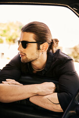 Obraz premium appealing sexy man with accessories in stylish black attire posing near his car and looking way