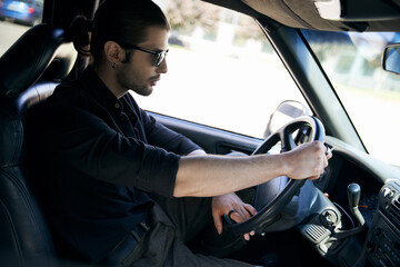 charming man with ponytail in black trendy outfit behind steering wheel of his car, sexy driver