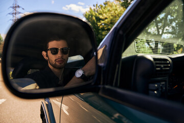 tempting elegant man with sunglasses in black stylish outfit looking in side mirror, sexy driver