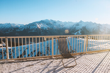 Balcony with chair overlooking the snow-capped mountains of the Zell am See ski resort in Austria. Sunny winter day, vacation in the Alps. Relaxing photo without people