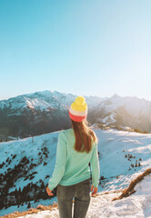 A young woman in a winter sports cap stands with her back against the backdrop of the Zell Am See...