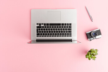 Overhead shot of laptop, photo camera, pen and small flower on pink background with copyspace....