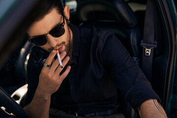 handsome sexy man with ponytail and accessories smoking cigarette behind steering wheel, sexy driver