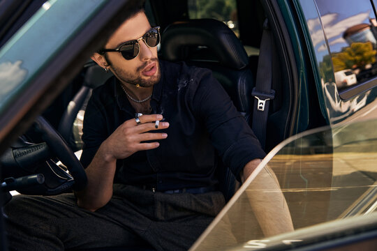 sexy male model in black shirt with sunglasses behind driving steering wheel and smoking cigarette