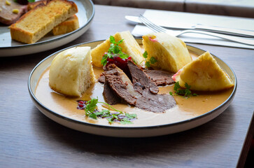 traditional Czech food served on a wooden table, cream sauce, dumpling, beef, cranberries, wild dear or beef meat