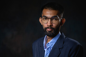 Portrait of young bearded man with glasses and looking at camera on dark background. - obrazy, fototapety, plakaty
