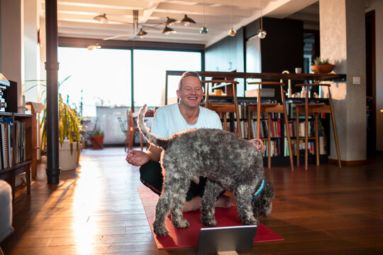 Man laughing as his dog interrupts his yoga session at home