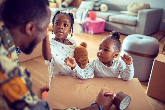 Father and daughters preparing a cardboard box for their toys at home