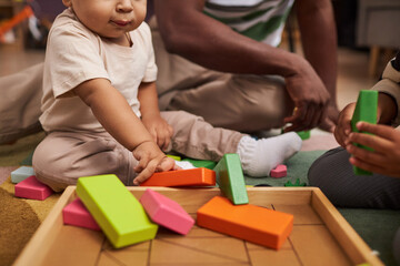Obraz premium Close up of cute baby playing with wooden toy bricks on floor at home with family, copy space